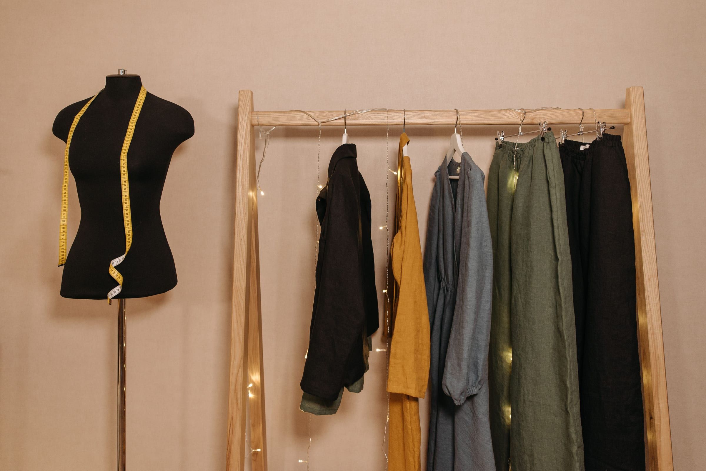A black dress form with a tape measure beside a wooden rail of linen clothes