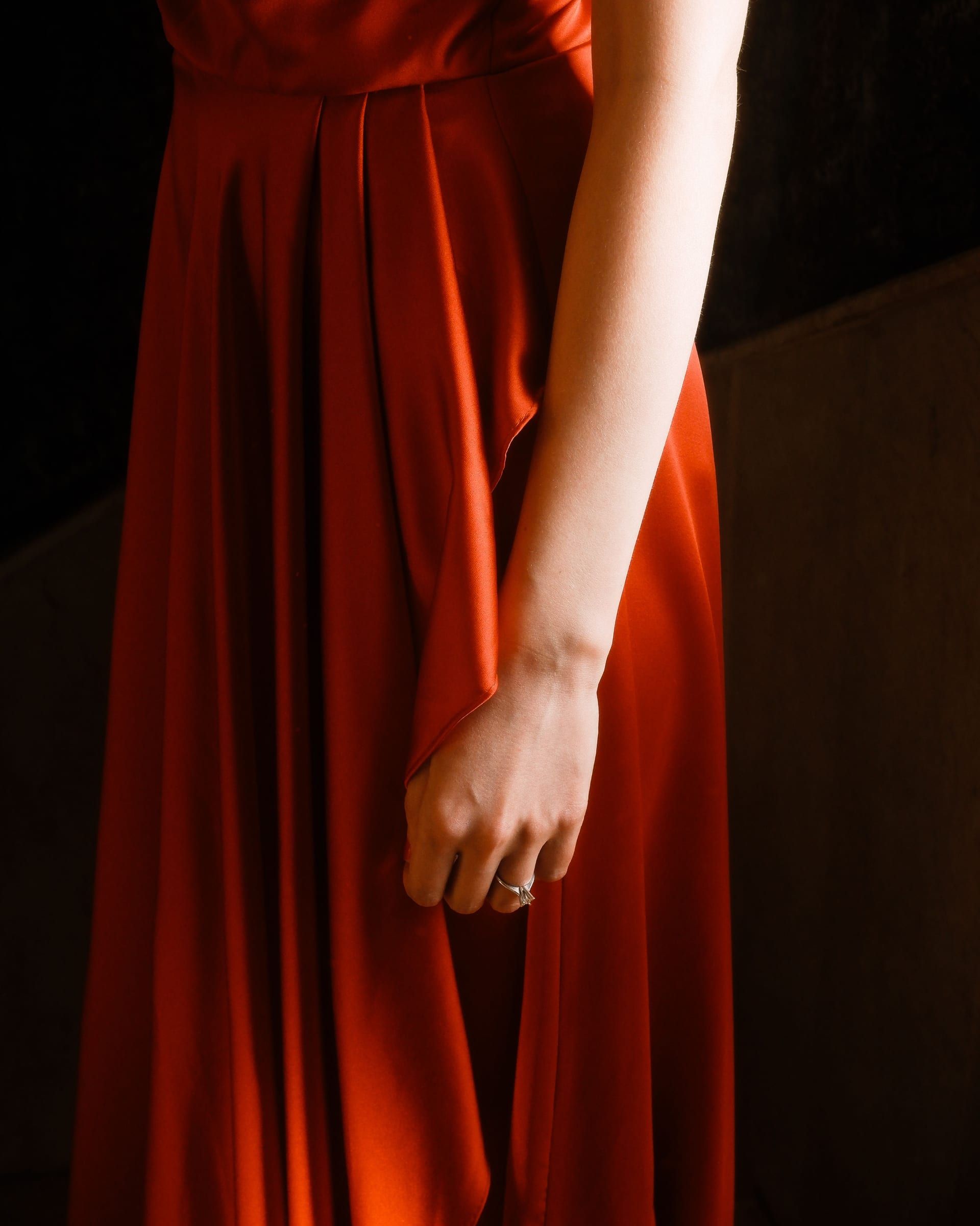 A rust-red satin evening gown with a draped skirt, seen from the shoulder to the hem