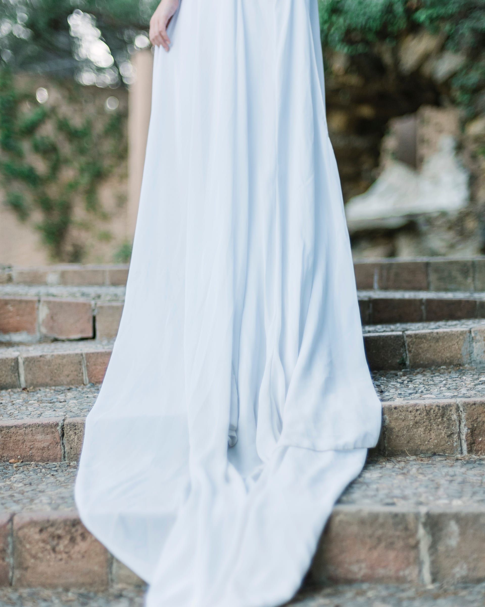 The back of a plain white wedding gown, its long train spilling down brick garden steps