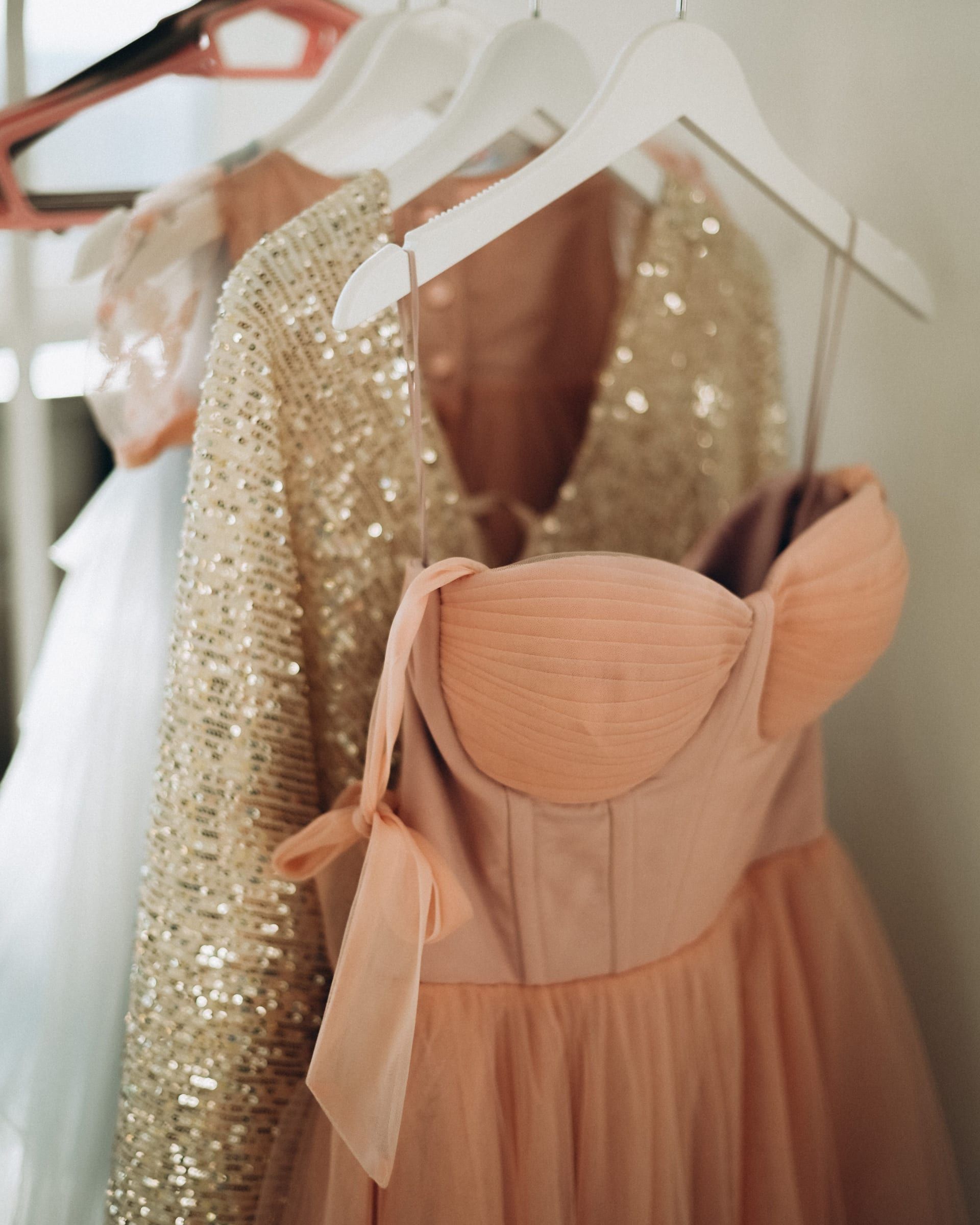 A blush tulle cocktail dress with a corset bodice beside a gold sequin dress, on white hangers