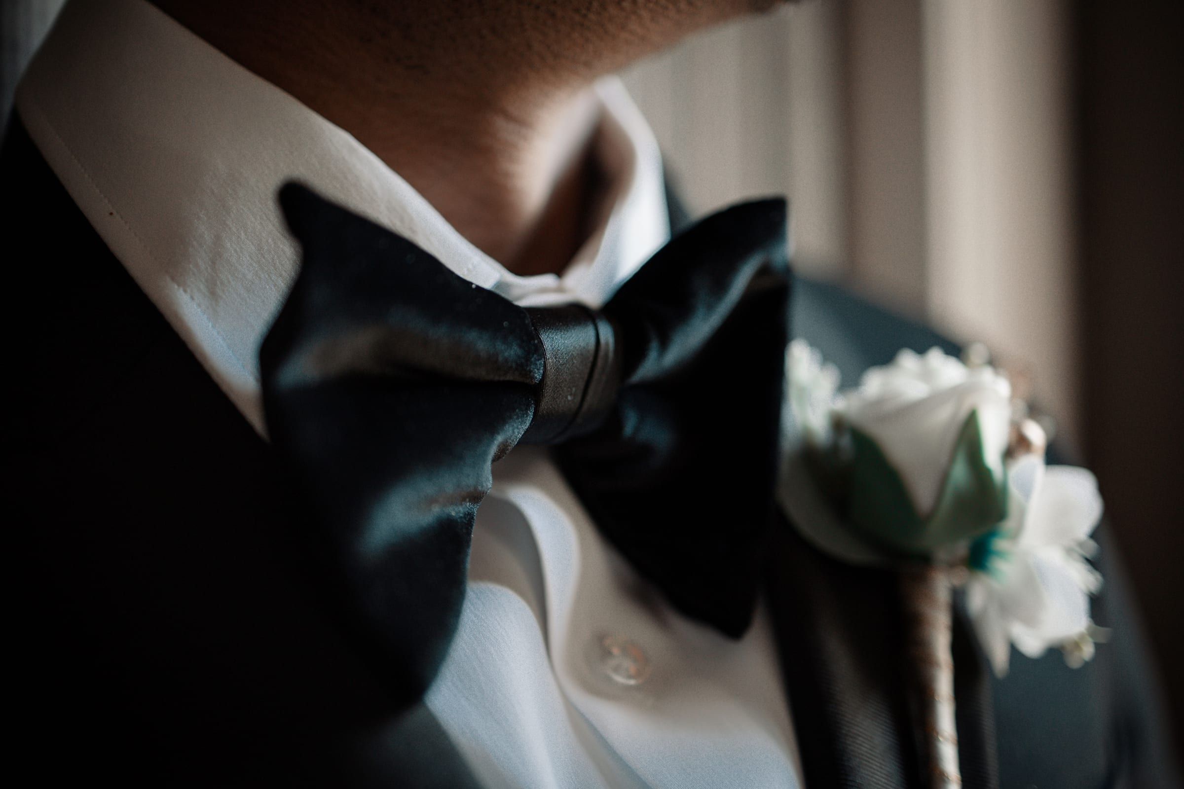 A black satin bow tie, a tuxedo lapel and a white rose boutonniere