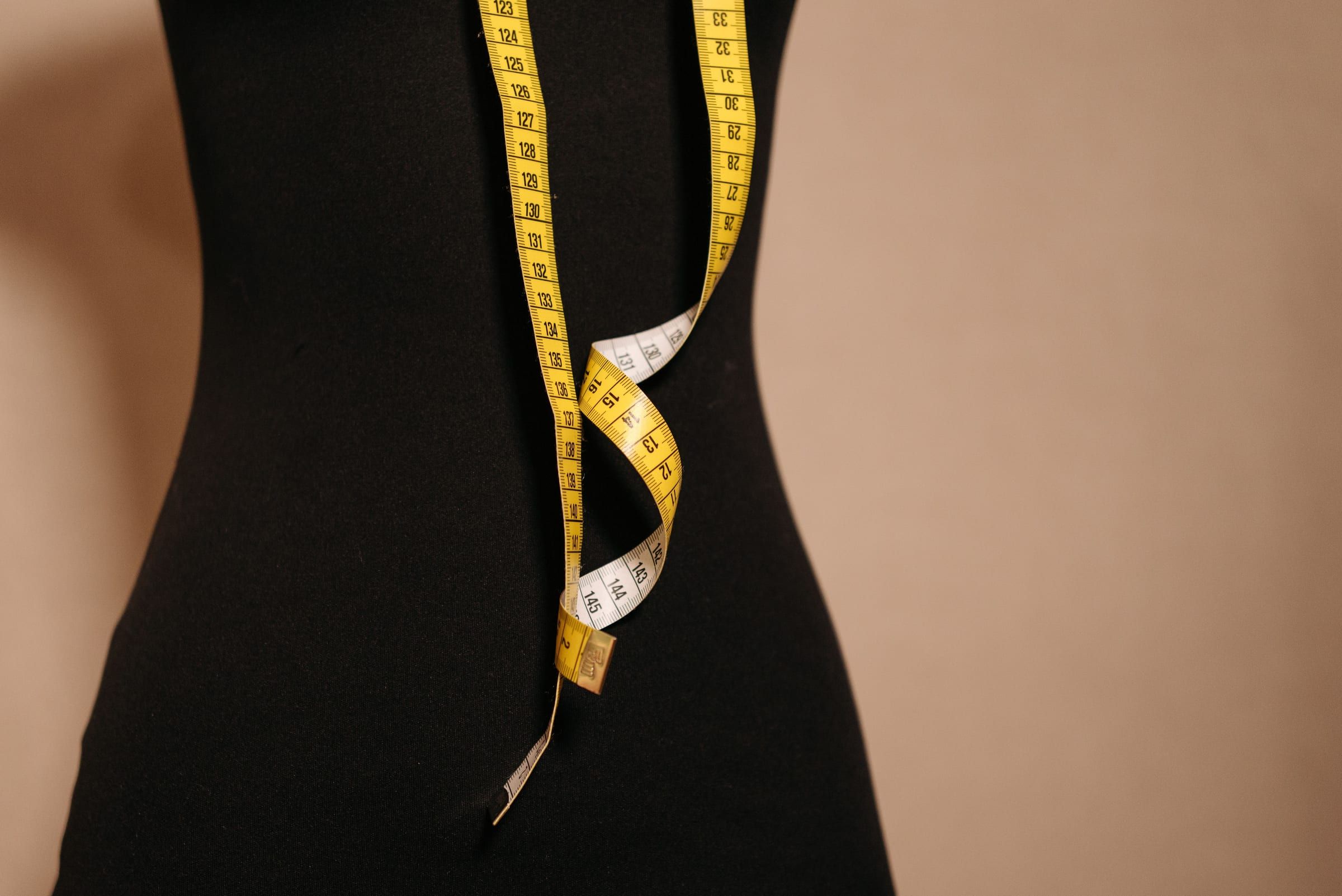 A yellow tape measure hanging over a black dress form