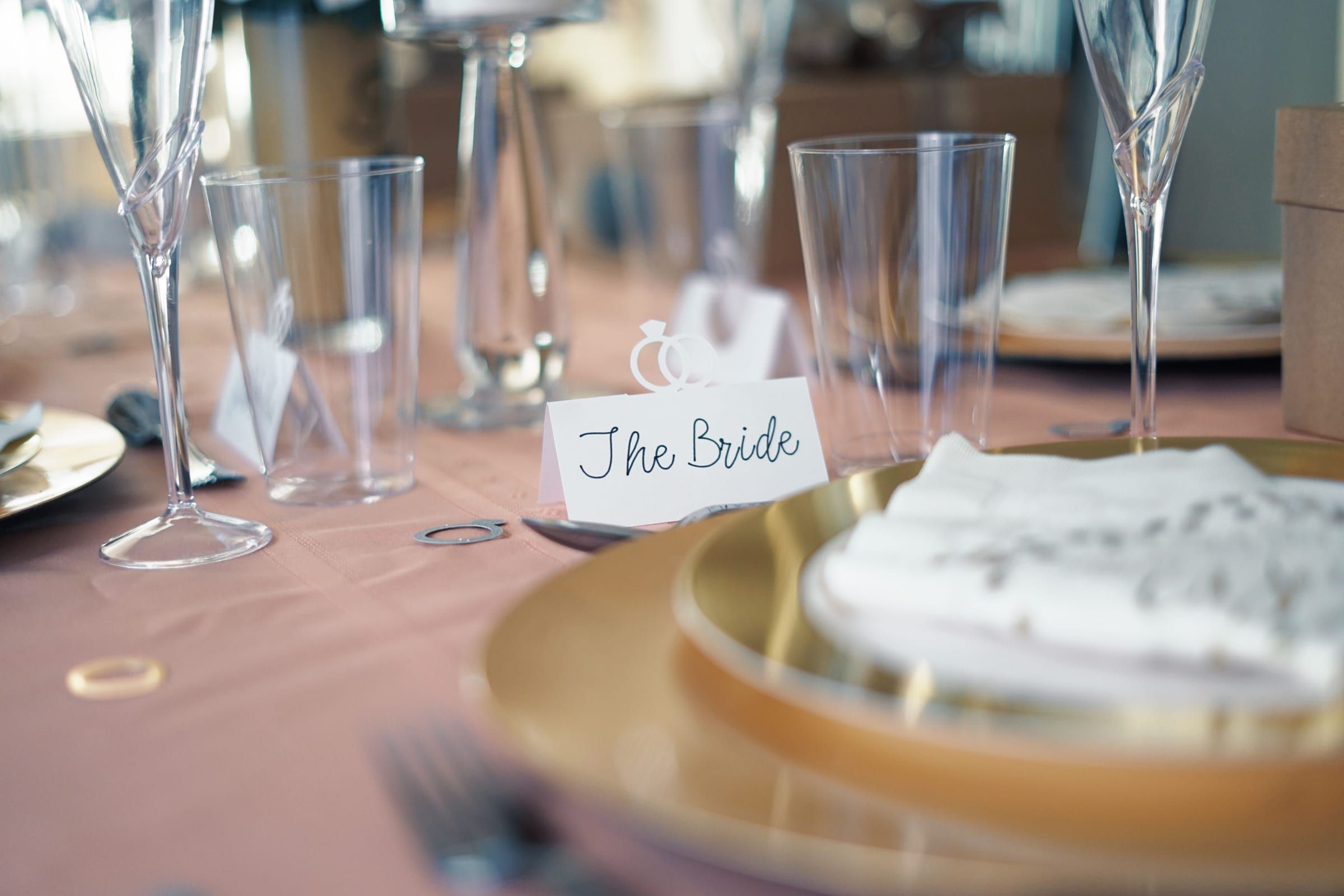 A reception table set with a gold charger, glassware and a handwritten place card for the bride
